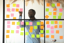 Focused African Businessman Checking Project Progress On Sticky Notes