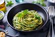 © annapustynnikova - Pasta spaghetti with pesto sauce and fresh basil leaves in black bowl. Grey background. Close up.