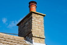 Large, English Cottage Style Brick Chimney Showing A Newly Installed Terracotta Pot Together With A Chimney Cover To Prevent Birds Nesting. Part Of The Roofing Can Also Be Seen.