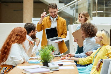 Joyful positive group of talented workers listen to bearded young man with note book, express attention, startup concept