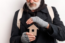 Unrecognizable Old Man Wearing Street Clothes Holding House Made Of Cardboard, Dream About Shelter. Isolated Over White Background
