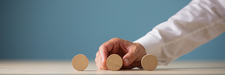 Wall Mural - hand of a businessman placing three blank wooden cut circles in a row