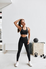 Wall Mural - Caucasian long-haired girl in black leggins and topic stretching body, arms. White gym background