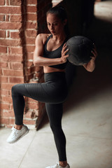 Wall Mural - Sportswoman stretching legs with help of balls. Caucasian Girl in black sportswears. Brickwall background