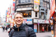 Tokyo, Japan Shibuya district and happy man tourist closeup in famous Koen dori shopping street in downtown city with colorful architecture in bokeh background