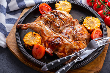 Wall Mural - Delicious roasted small  chicken  with corn and tomatoes on frying pan. Closeup