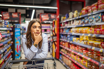 young woman staying confused in grocery store. confused woman doesnt know what to buy. young woman w