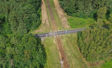 Aerial Drone Perspective View On Railroad Crossing With Asphalt Road In The Forest With Car Passing