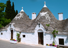 Street With Unique White Buildings With Conical Roof Called "Trulli" And Religion Symbols On It In Alberobello Small Town And Comune Of The Metropolitan City Of Bari, Puglia, Southern Italy. 