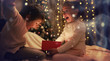 Family on Christmas eve at fireplace. Kids opening Xmas presents. Children under Christmas tree with gift boxes. Decorated living room with traditional fire place. Cozy warm winter evening at home.