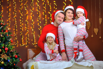 Portrait of a happy family in pajamas and santa claus hats lie in the bedroom on the bed hugging and smiling