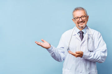 Cheerful mature doctor posing and smiling at camera, healthcare and medicine. Isolate on blue background.