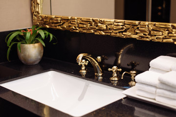 A stack of fresh white towels in the hotel's luxurious bathroom. A gold faucet, mirror and marble sink in a public restroom of an expensive building