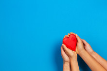 Adult And Child Hands Holding Red Heart Over Blue Background. Love, Healthcare, Family, Insurance, Donation Concept