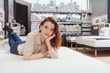 © Ihor - Charming young woman lying on orthopedic bed at furniture store, smiling to the camera
