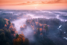 Aerial View Of Foggy Forest At Colorful Sunrise In Autumn. Amazing Landscape With Colorful Trees In Fog, River, Field And Red Sky With Sun In The Morning. Fall Colors. Fairy Scenery. Top View. Nature