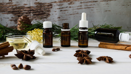 composition of natural oils, glass bottles with oil, cinnamon sticks, anise, pine nuts on a white wooden table on a background of green branches