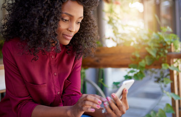 Wall Mural - Smiling African American woman sitting outside reading a text message