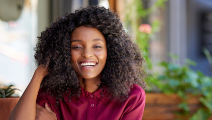 Wall Mural - Laughing African American woman sitting at a cafe table outside