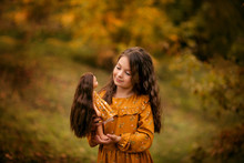 Portrait Of A Happy Girl Of 8-9 Years Old In Nature In The Autumn In The Park, The Child Has A Doll In Her Hands