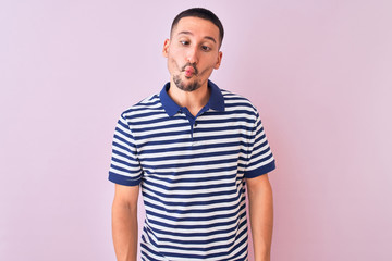 Poster - Young handsome man wearing nautical striped t-shirt over pink isolated background making fish face with lips, crazy and comical gesture. Funny expression.