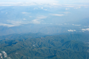  Top view of a long row of wind farms installed along the ridge of the mountain. Many white wind farms in the hills of the mountains against the backdrop of mountainous terrain and clouds.