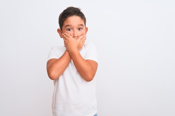 Canvas Print - Beautiful kid boy wearing casual t-shirt standing over isolated white background shocked covering mouth with hands for mistake. Secret concept.