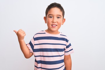 Poster - Beautiful kid boy wearing casual striped t-shirt standing over isolated white background smiling with happy face looking and pointing to the side with thumb up.