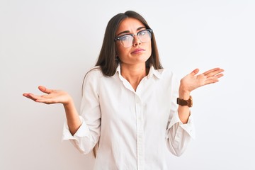 Poster - Young beautiful businesswoman wearing glasses standing over isolated white background clueless and confused expression with arms and hands raised. Doubt concept.