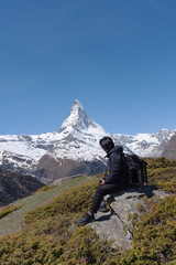 Wall Mural - a man with backpack sitting on rock with matterhorn mountain view in switzerland. travel lifestyle a