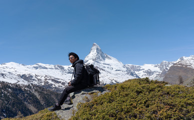 Wall Mural - a man with backpack sitting on rock with matterhorn mountain view in switzerland. travel lifestyle a