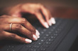 © bibi - Isolated close-up of ethnic hands typing on black keyboard with white letters on wooden table
