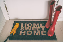 Autumn Rain Boots On Entrance Door Mat At Front Of House With Wet Umbrella Welcome Rug On Wooden Floor For Shoes And Winter Boots. New House, Condo Apartment Fall Winter Concept.