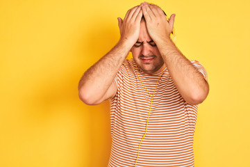 Poster - Young man listening to music using headphones standing over isolated yellow background suffering from headache desperate and stressed because pain and migraine. Hands on head.