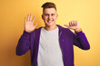 © Krakenimages.com - Young handsome man wearing purple sweatshirt standing over isolated yellow background showing and pointing up with fingers number six while smiling confident and happy.