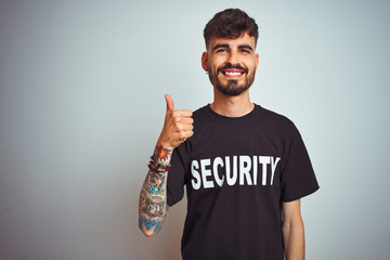 Sticker - Young safeguard man with tattoo wering security uniform over isolated white background doing happy thumbs up gesture with hand. Approving expression looking at the camera showing success.