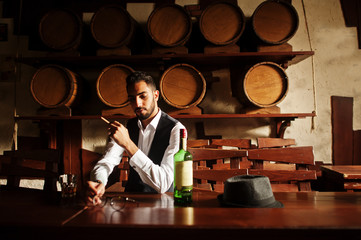 Wall Mural - Handsome well-dressed arabian man with glass of whiskey and cigar posed at pub.