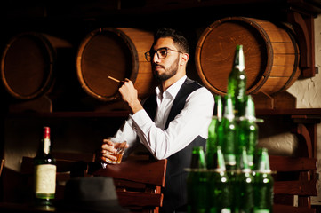 Wall Mural - Handsome well-dressed arabian man with glass of whiskey and cigar posed at pub.