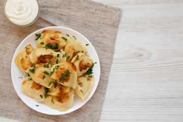 Wall Mural - Homemade traditional polish fried potato pierogis on a white plate with sour cream, top view. From above, flat lay, overhead. Copy space.