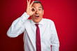 © Krakenimages.com - Handsome middle age businessman standing over isolated red background doing ok gesture shocked with surprised face, eye looking through fingers. Unbelieving expression.