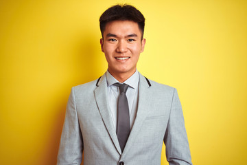 Asian chinese businessman wearing suit and tie standing over isolated yellow background with a happy and cool smile on face. Lucky person.