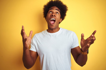 Sticker - American man with afro hair wearing white t-shirt standing over isolated yellow background crazy and mad shouting and yelling with aggressive expression and arms raised. Frustration concept.