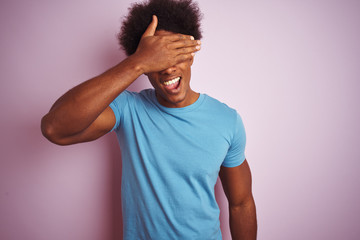 Poster - African american man with afro hair wearing blue t-shirt standing over isolated pink background smiling and laughing with hand on face covering eyes for surprise. Blind concept.