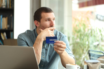 Pensive man holding a credit card thinking looking away