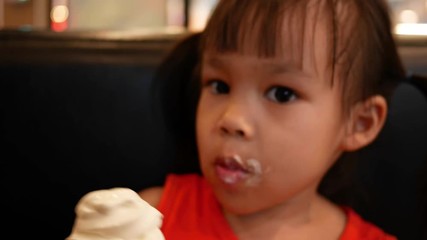 adorable little asian child girl holding and eating ice cream with cone in restaurant.