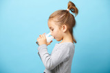 Child girl drinks milk without lactose, sideways portrait against blue isolated.