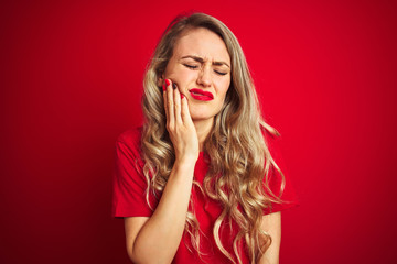 Poster - Young beautiful woman wearing basic t-shirt standing over red isolated background touching mouth with hand with painful expression because of toothache or dental illness on teeth. Dentist concept.