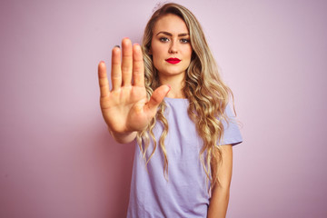 Canvas Print - Young beautiful woman wearing purple t-shirt standing over pink isolated background doing stop sing with palm of the hand. Warning expression with negative and serious gesture on the face.