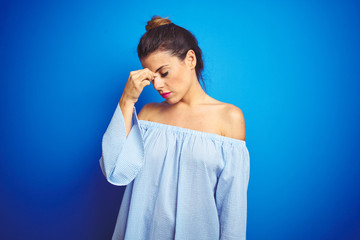 Poster - Young beautiful woman wearing bun hairstyle over blue isolated background tired rubbing nose and eyes feeling fatigue and headache. Stress and frustration concept.