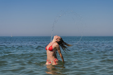 Young beautiful girl sprays water with hair in the form of a circle in the sea